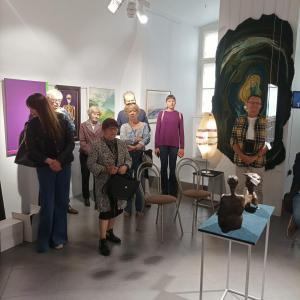 W przestrzeni wystawy „Splecione światy 80 lat ZPAP w Bielsku-Białej” licznie zgromadzeni słuchacze stoją obok eksponatów, uważnie przyglądając się dziełom sztuki. Goście wystawy, stojąc wśród dzieł, zdają się chłonąć zarówno wizualne, jak i merytoryczne 