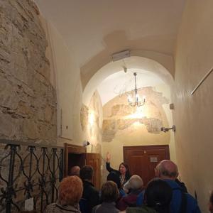 na zdjęciu P. Bożena Chorąży wskazująca na ściany zamkowe, przed nią tłum ludzi zwrócony w jej stronę, w tle korytarz zamkowy