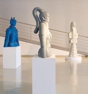 Na zdjęciu trzy rzeźby, przedstawiające postacie, postawione na białych kolumnach. Pierwsza rzeźba , stojąca po lewej stronie jest w kolorze niebieskim, środkowa w kolorze szarym, ta z prawej - w kolorze białym. Rzeźby są fragmentem wystawy czasowej, znaj