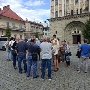 Na zdjęciu znajduje się spora grupa ludzi w różnym wieku. Oosby te stoją przed Kościołem Św. Mikołaja.