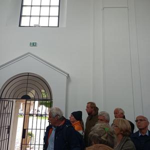 na środku zdjęcia P. Bogusław Chorąży, opowiadający o wnętrzu kaplicy, obok niego ludzie zwróceni w jego stronę, w tle kaplica zamkowa