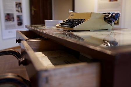 Zbliżenie na biurko i maszynę do pisania, dwie szuflady biurka wysunięte.