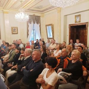 Na zdjęciu widoczny jest tłum ludzi siedzących na krzesłach w eleganckim salonie muzycznym. Wszyscy są wpatrzeni i zasłuchani w opowieści dziennikarza Bogdana Frymorgena, który stojąc przed nimi, z pasją dzieli się swoimi historiami.