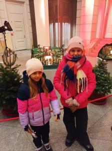 Dwoje dzieci przed choinkami i szopką.