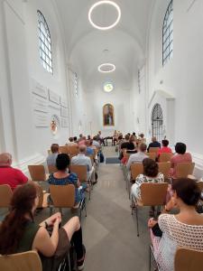 zdjęcie wnętrza kaplicy wykonane z tyłu, na krzesłach goście słuchający przemowy