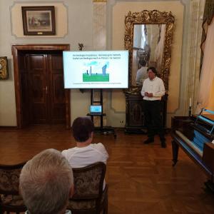 W salonie muzycznym w Bielsku-Białej, podczas wykładu w ramach EDA (Europejskie Dni Archeologii w Bielsku-Białej), bielski archeolog prowadzi pasjonującą prelekcję. Na dużym telewizorze w tle wyświetlana jest prezentacja wizualna, która ilustruje omawiane