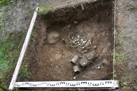 Wykop archeologiczny w lesie. Wewnątrz wykopu znalezione przedmioty - ozdoby