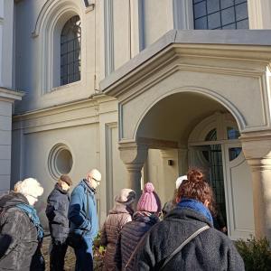 grupa ludzi ubranych na zimowo - zbliżająca się do drzwi kaplicy zamkowej, w tle ściana zewnętrzna kaplicy zamkowej