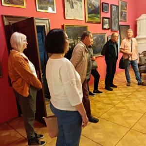Zdjęcie przedstawia sześć stojących osób, które przybyły na spotkanie z Teresą Dudek Bujarek. W tle widoczne są obrazy wiszące na ścianach w sali im. A. Bunscha