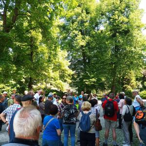 Na nowym zdjęciu widzimy znacznie większą grupę pasjonatów archeologii, zgromadzoną w lesie wokół bielskich archeologów. Wszyscy uczestnicy spaceru są skupieni na wykładzie, który odbywa się w tym malowniczym, naturalnym otoczeniu.