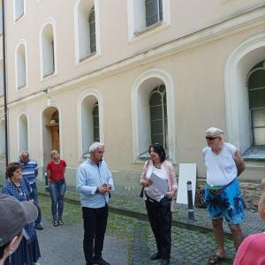 Na zdjęciu widzimy grupę bielskich archeologów, którzy prowadzą interesujące spotkanie spacerowe. Mężczyzna w jasnoniebieskiej koszuli, z pasją i zaangażowaniem, tłumaczy zebranym uczestnikom zagadnienia związane z archeologią. Jego mowa ciała oraz wyraz 