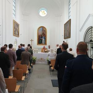 Na zdjęciu widzimy grupę ludzi w skupieniu, którzy zwróceni są w stronę ołtarza, uczestnicząc w nabożeństwie. Msza Święta jest sprawowana przez biskupa Gregera, który przewodzi liturgii w kaplicy św. Anny. W tle widać ozdobne obrazy, umiejscowione po obu 