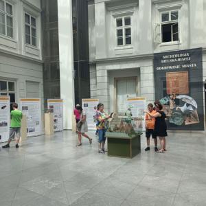 Zdjęcie przedstawia wnętrze Atrium. Na środku znajduje się przeszklona gablota a w niej makieta Zamku. Wokół gabloty stoi grupka ludzi w różnym wieku. W tle duży, czarny baner zapowiadający wystawę.